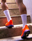 Person läuft mit All White Socken und orangenen Laufschuhe eine Treppe hoch