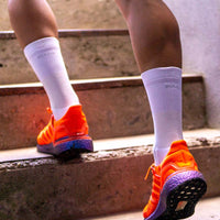 Person läuft mit All White Socken und orangenen Laufschuhe eine Treppe hoch