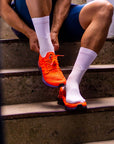 Person sitzt auf einer Treppe und zieht sich All White Socken und orangene Laufschuhe an
