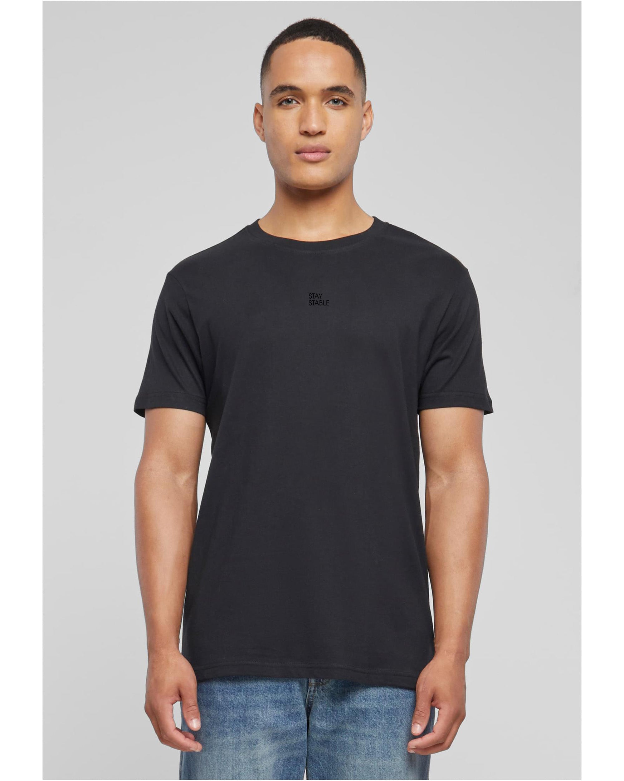 Person mit schwarzem basic T-Shirt bekleidet von vorne mit schwarzem Stay Stable Print mittig auf der Brust